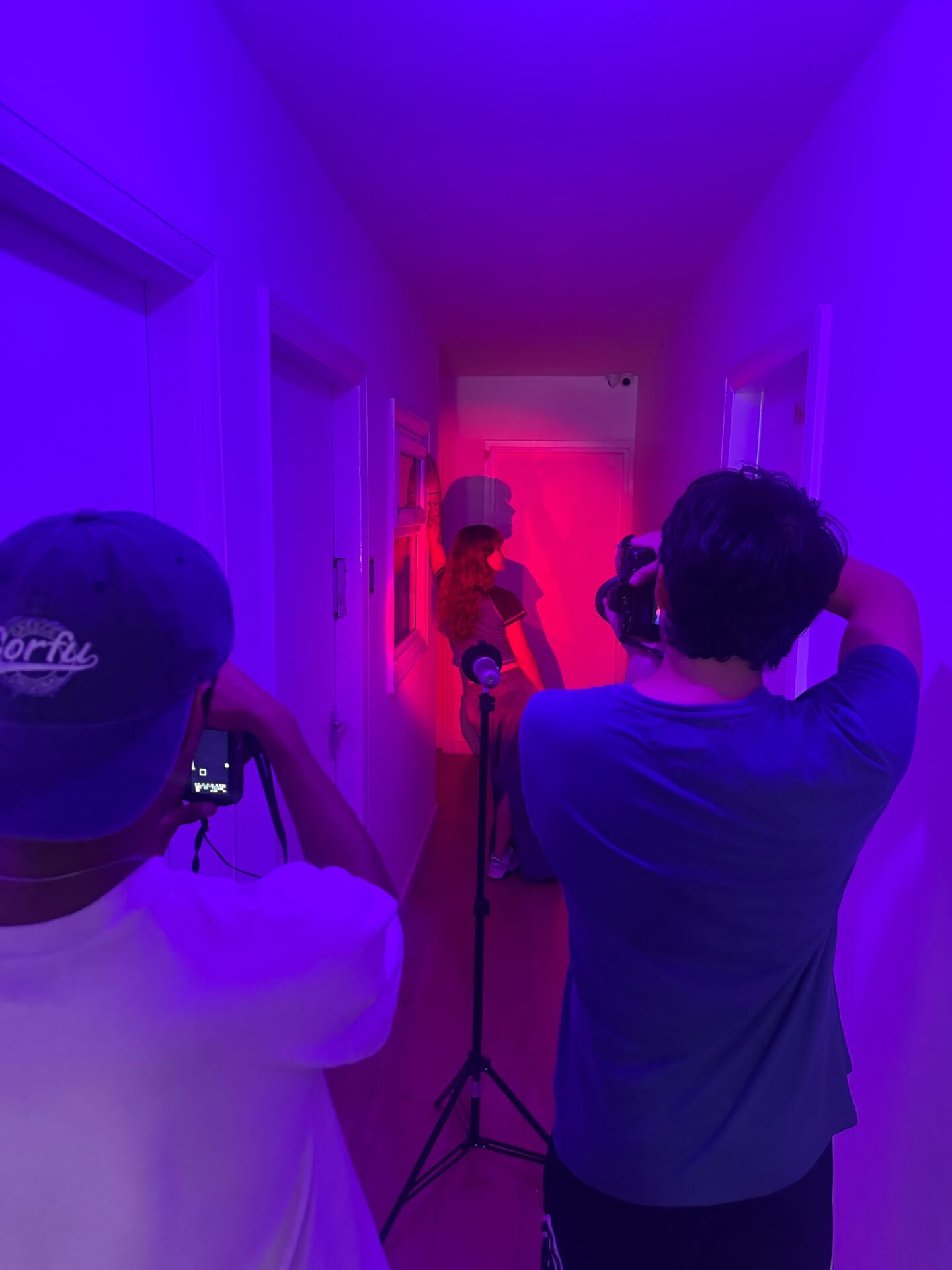Two photographers shooting a model at the end of a corridor lit purple and pink