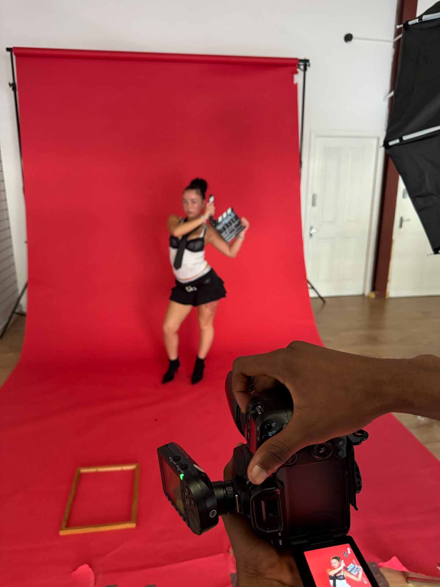 Model holding a clapperboard on the red backdrop with a camera in the foreground