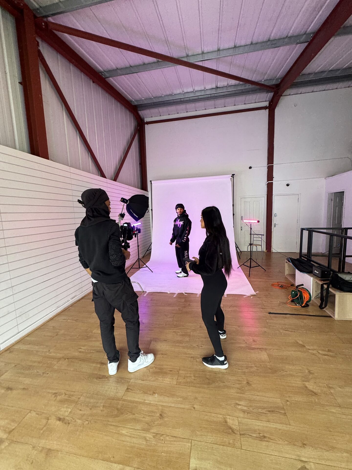 Wide view of the room with crew watching a model on the white backdrop lit with pink tube lights