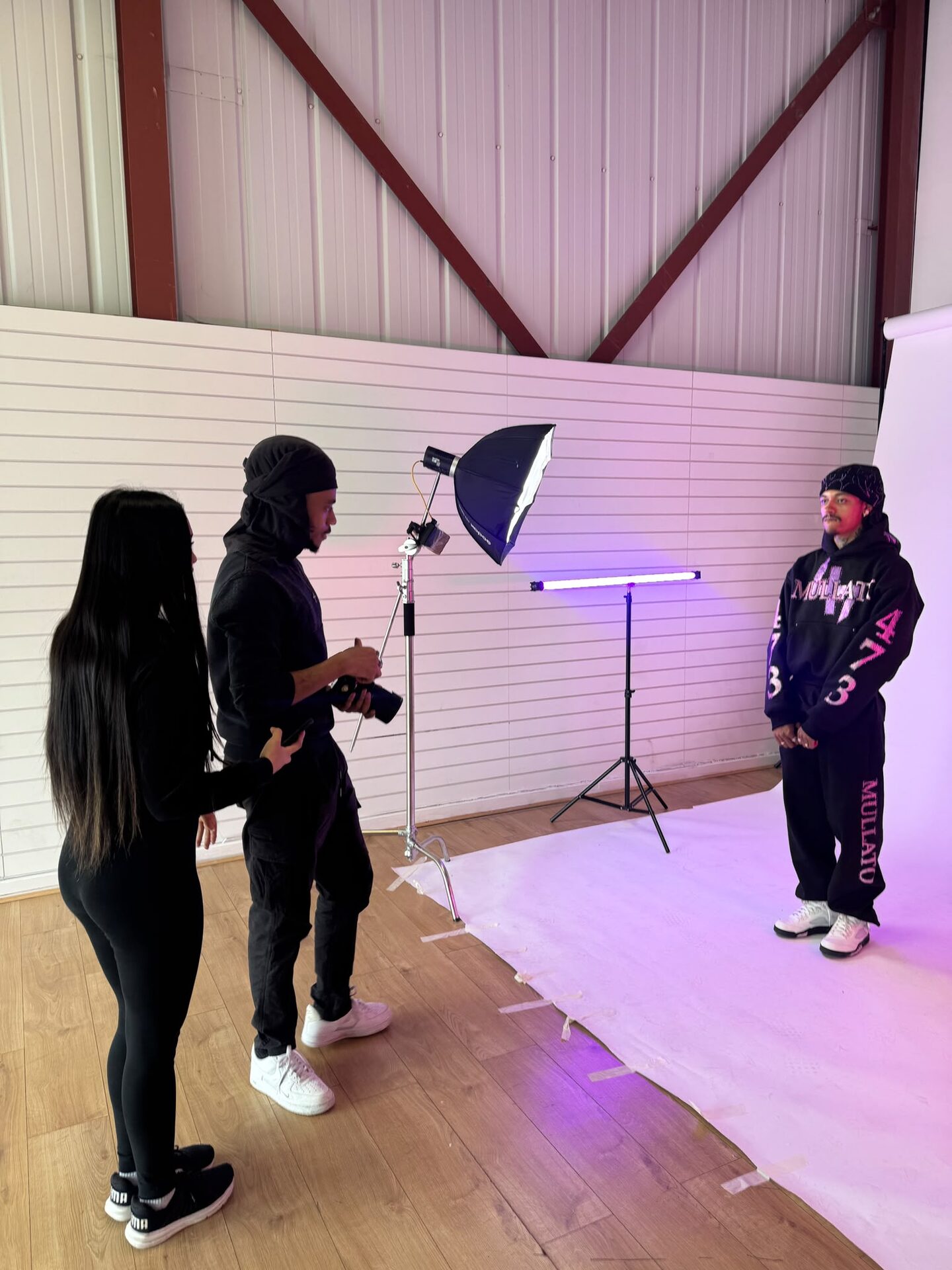 Crew directing a model in a black hoodie on the white backdrop under a purple tube light
